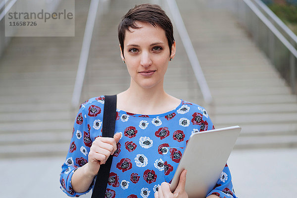 Porträt einer mittleren erwachsenen Frau  die im Freien steht und Tasche und Laptop hält