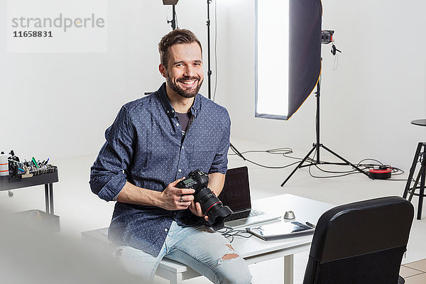 Porträt eines männlichen Fotografen  der im Fotostudio am Schreibtisch sitzt