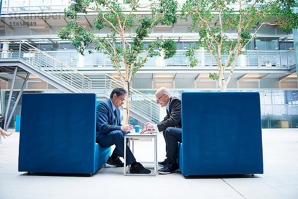 Zwei Geschäftsleute bei einer Diskussionsrunde in Büro-Atrium-Sesseln