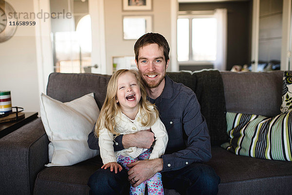 Porträt eines auf dem Sofa sitzenden Mannes mit Tochter auf dem Knie
