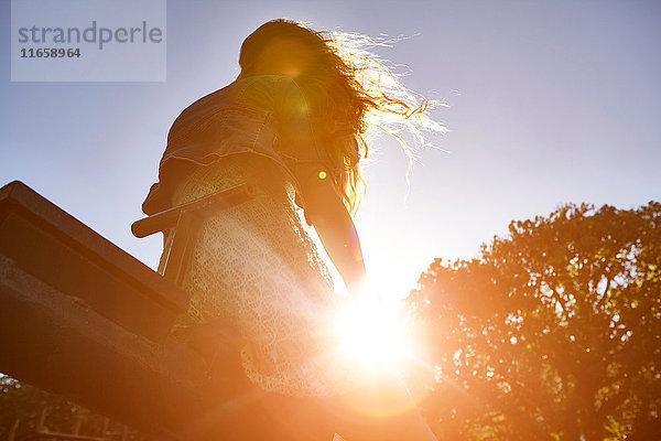 Mädchen sitzt auf einer Wippe  helles Sonnenlicht scheint durch Bäume  niedriger Blickwinkel