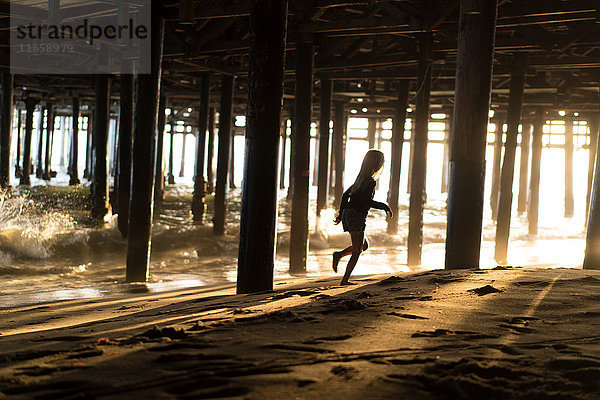 Silhouette eines Mädchens  das vor sich überlappenden Wellen unter dem Pier von Santa Monica rennt  Kalifornien  USA