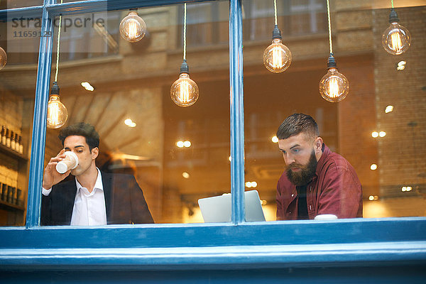 Fensteransicht von Geschäftsleuten  die Kaffee trinken und Laptop im Cafe benutzen