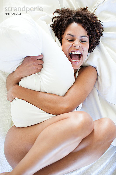 Draufsicht einer nackten Frau  die auf einem Bett liegt und ein Kissen umarmt