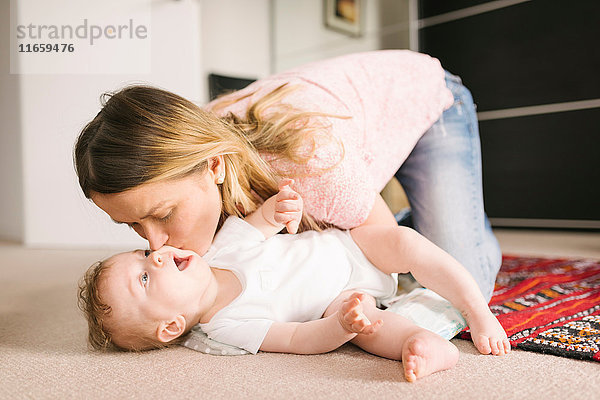 Mutter küsst Baby auf Teppich