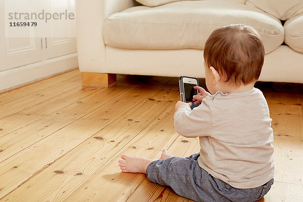 Kleiner Junge sitzt auf dem Boden und nutzt den Touchscreen eines Smartphones