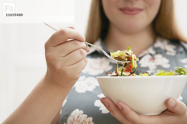 Junge Frau isst Schüssel mit Salat.