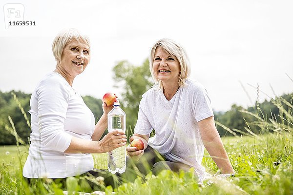 Zwei Frauen sitzen im Gras mit Äpfeln und Wasser.