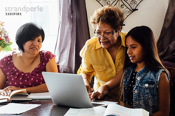 Mutter und Großmutter helfen Mädchen mit dem Laptop bei den Hausaufgaben