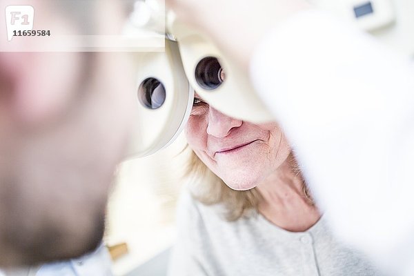 Ein Optiker führt einen Sehtest bei einer älteren Frau mit einem Phoropter in einem Optikerladen durch.