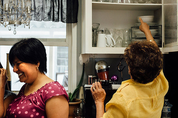 Frau in der Küche stellt Geschirr in den Küchenschrank