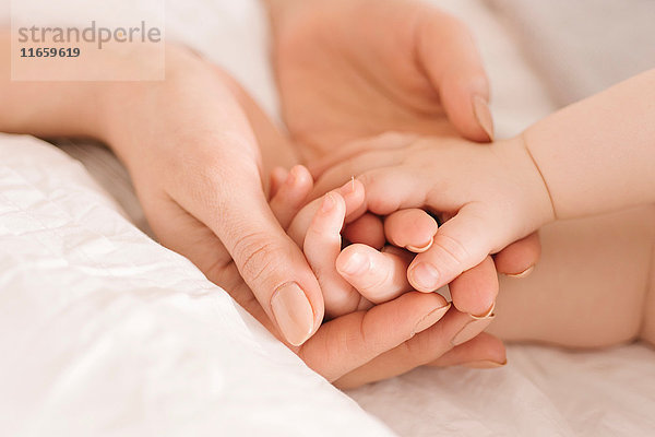 Mutter hält die Hände des Babys auf dem Bett