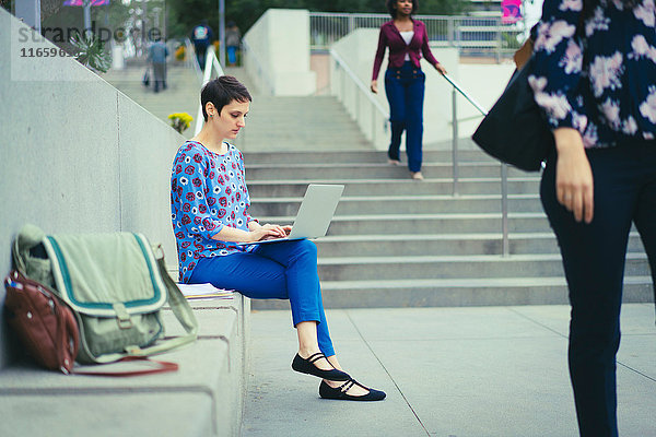 Junge Frau sitzt im Freien und benutzt einen Laptop