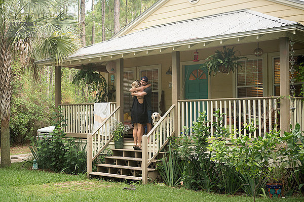 Junges Paar mit Labrador umarmt sich auf der Veranda