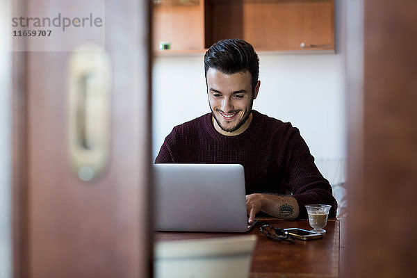 Junger Mann sitzt mit Laptop am Tisch