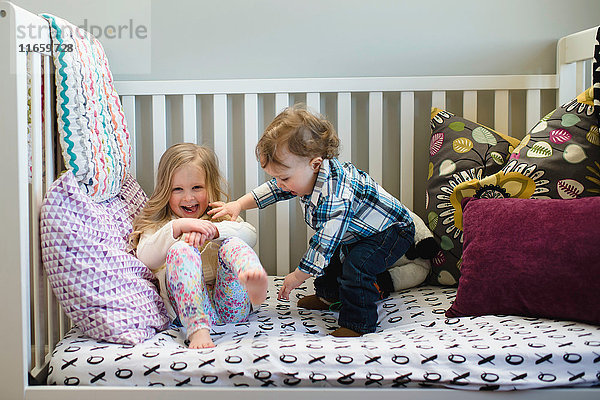 Männliches Kleinkind und Schwester spielen im Tagesbett