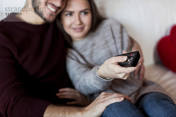 Junges Paar entspannt sich auf dem Sofa  sieht fern  junge Frau hält Fernbedienung