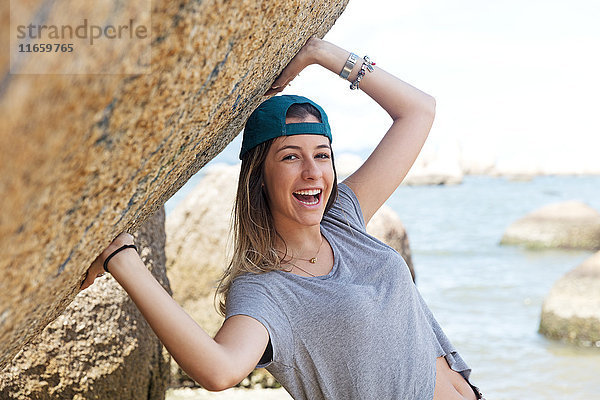 Porträt eines Teenager-Mädchens auf Felsen am Meer  das lächelnd in die Kamera schaut