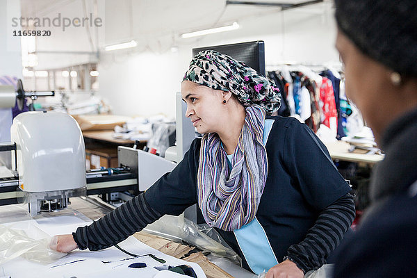 Fabrikarbeiterinnen entfernen geschnittene Textilien von der Musterschneidemaschine in einer Bekleidungsfabrik