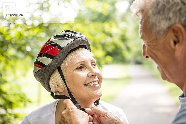 Ältere Frau mit Fahrradhelm  älterer Mann hilft ihr.