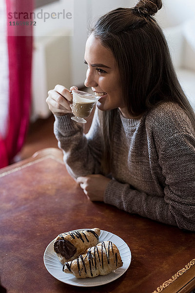 Junge Frau sitzt am Tisch  trinkt Kaffee  Gebäck auf dem Tisch vor ihr