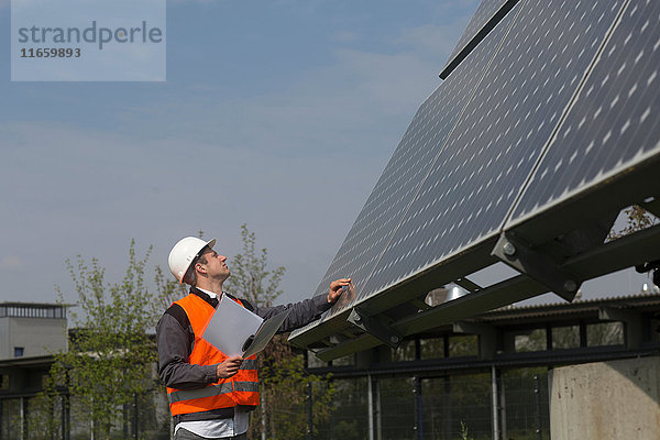 Junger männlicher Ingenieur mit digitalem Tablett schaut zu Sonnenkollektoren auf