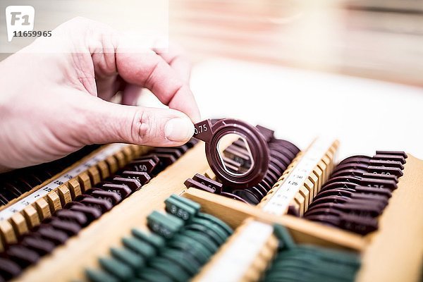 Nahaufnahme einer Hand  die ein Objektiv aus einem Gestell hält  das für einen Sehtest verwendet wird.