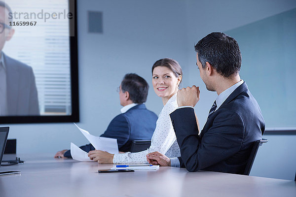 Geschäftsfrau schaut bei Büro-Telefonkonferenz über ihre Schulter