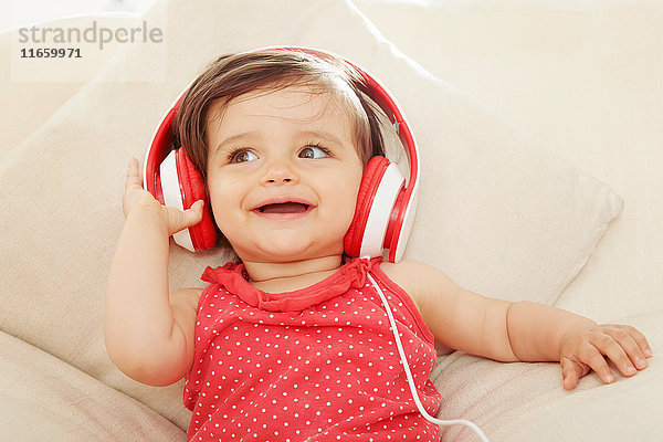 Kleines Mädchen auf dem Sofa hört rote Kopfhörer