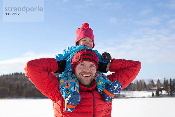 Vater trägt kleinen Sohn auf den Schultern  in schneebedeckter Landschaft