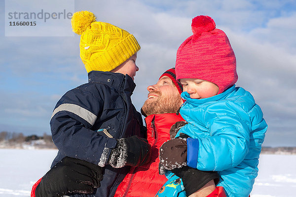 Vater hält zwei Söhne  in schneebedeckter Landschaft