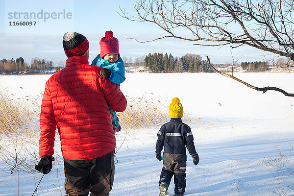 Vater und zwei Söhne spazieren in schneebedeckter Landschaft  Rückansicht