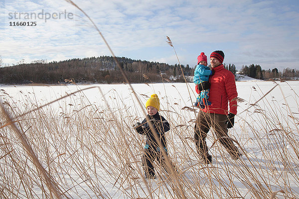 Vater geht mit zwei Söhnen in schneebedeckter Landschaft spazieren