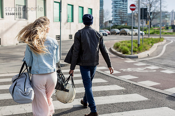 Junger Mann und junge Frau  überqueren die Straße mit Laderäumen  Rückansicht