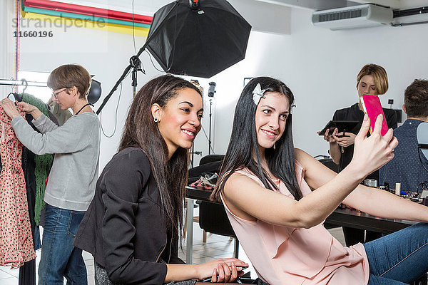 Zwei Modemodels beim Smartphone-Selfie im Fotografenstudio