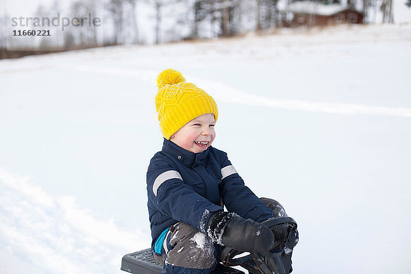 Junge sitzt auf Schlitten in schneebedeckter Landschaft