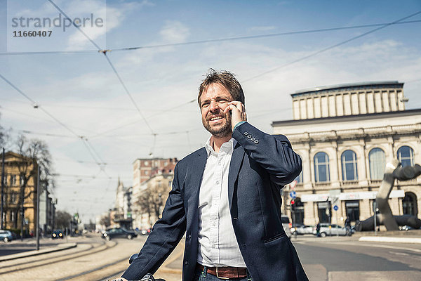 Geschäftsmann mit Fahrrad macht Smartphone-Anruf in der Stadt