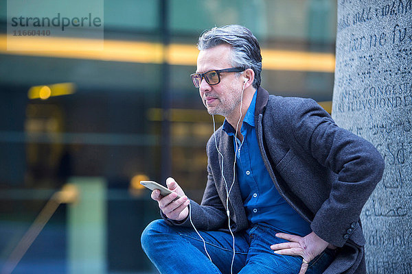 Mann mit Smartphone und Ohrstöpseln im Freien