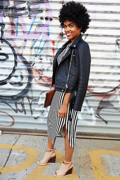 Stadtporträt einer jungen weiblichen Mode-Bloggerin mit Afro-Haaren an einer Graffiti-Wand  New York  USA