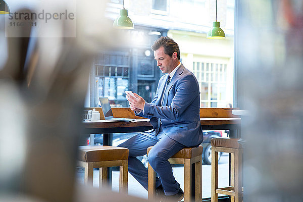 Der reife Geschäftsmann schaut sich das Smartphone im Restaurant an.