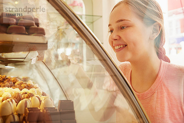 Mädchen in Bäckerei schaut lächelnd auf Kuchen in der Vitrine