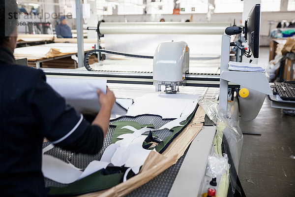Rückansicht eines Fabrikarbeiters  der geschnittene Textilmuster von der Musterschneidemaschine in einer Bekleidungsfabrik entfernt