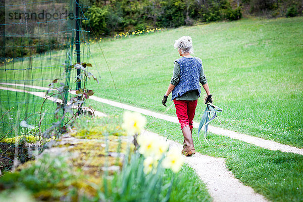 Rückansicht einer Frau  die Lauch am Gartenweg trägt