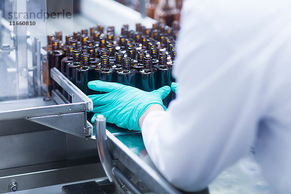 Arbeiter ordnen Flaschen auf einem Förderband in der Produktionslinie einer pharmazeutischen Fabrik an  mittlerer Abschnitt