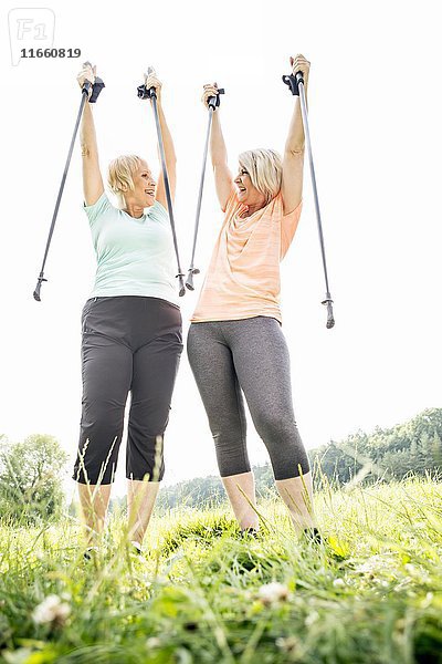 Zwei Frauen mit in die Luft erhobenen Wanderstöcken.