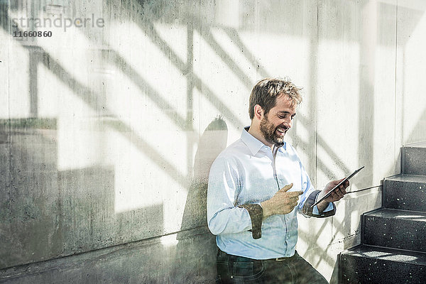 Geschäftsmann im Bürotreppenhaus schaut auf digitales Tablet