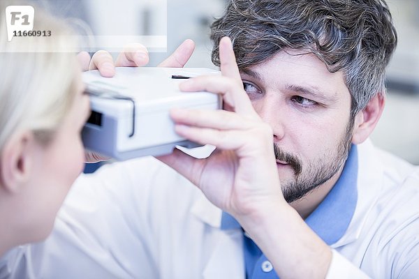 Optiker  der einen Sehtest bei einer jungen Frau durchführt.