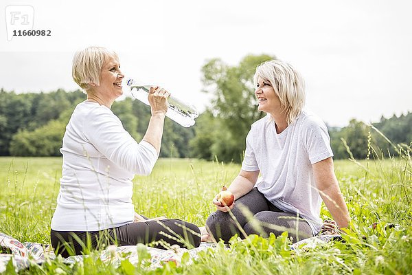 Zwei Frauen sitzen im Gras  eine trinkt Wasser.