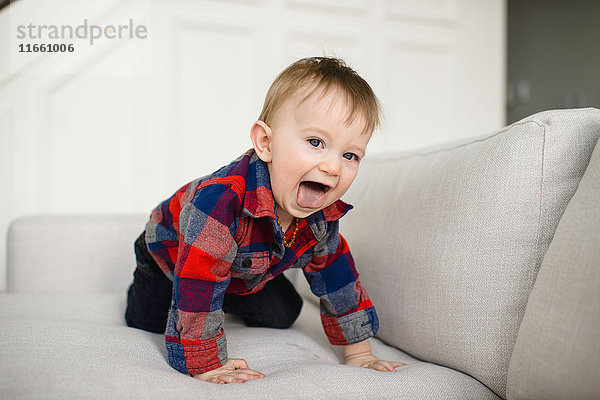 Porträt eines männlichen Kleinkindes  das auf dem Sofa krabbelt und die Zunge herausstreckt