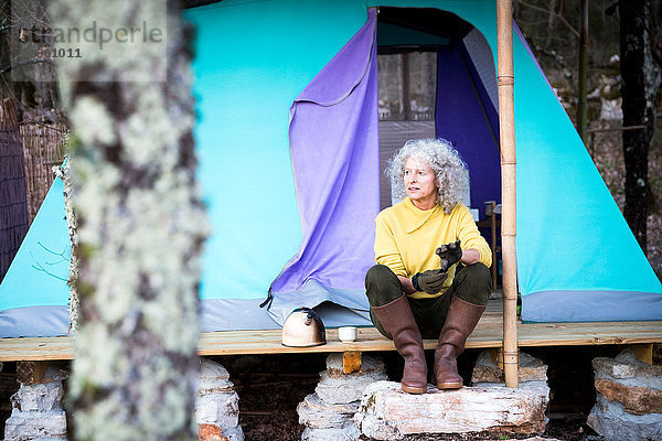 Reife Frau sitzt auf einer bewaldeten Camping-Veranda